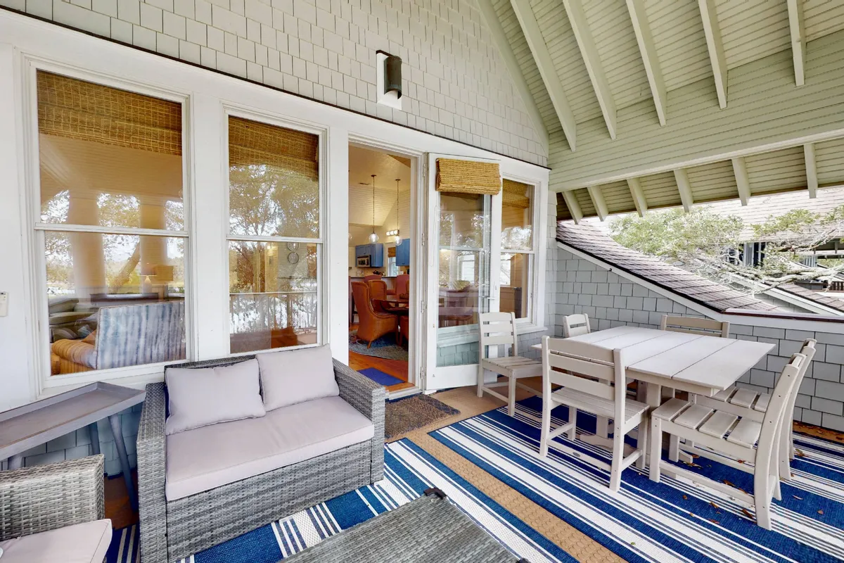 A relaxed exterior seating area with a dining table, textured rugs, and comfortable chairs, bathed in serene morning light. It's set up for outdoor dining and socializing, with vistas that suggest sunset views.