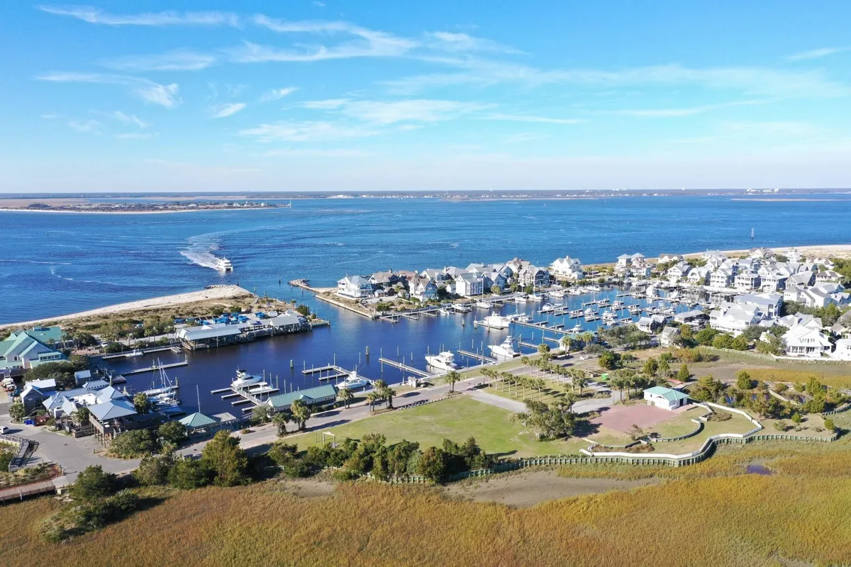 A scenic view of the marina, with boats docked along the waterfront, leafy green landscape, and waterfront homes in the background. The peaceful blue water and open sky evoke the island's coastal charm, perfect for adventures and leisurely days.