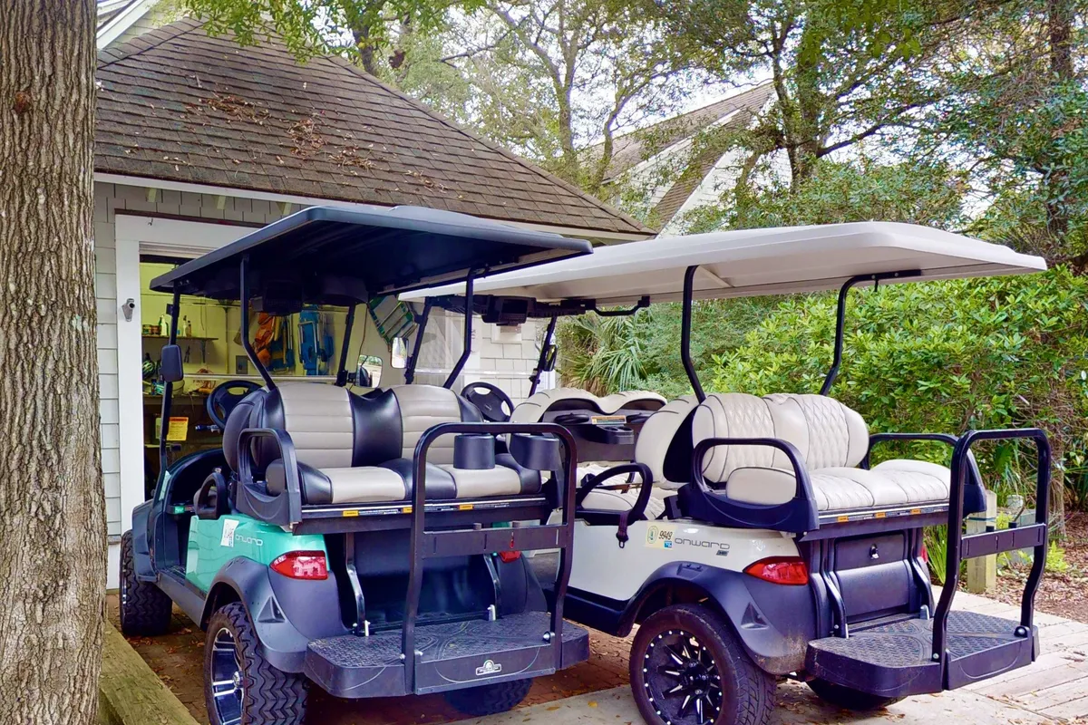 This image features a garage area with multiple golf carts parked in front, surrounded by lush foliage. The setting suggests readiness for adventure and easy access to on-island transportation.