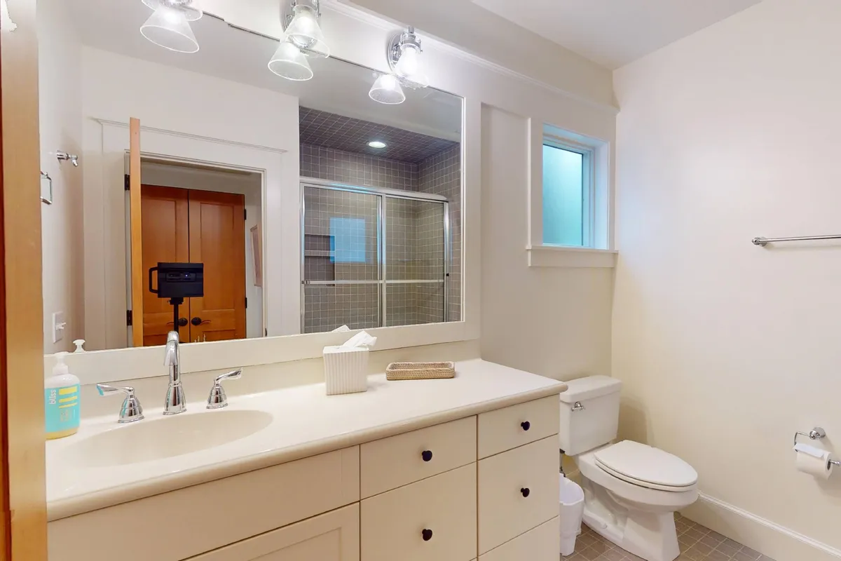 A calm and serene bathroom with a vanity and sink, large mirror, and a glass shower enclosure. The space is modern and fresh, offering a relaxing private area for self-care routines.