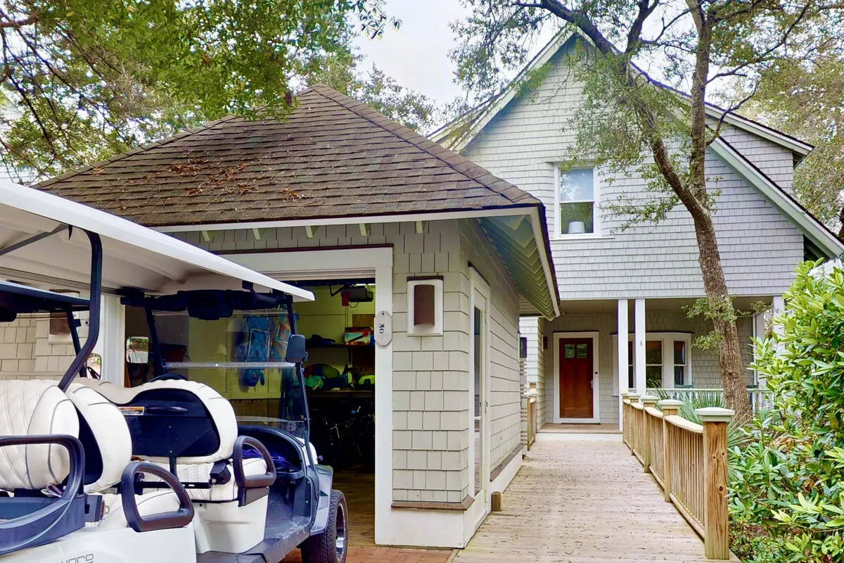 An exterior scene featuring a golf cart parked on a wooden pathway leading to the cottage's welcoming front entrance, surrounded by natural greenery.