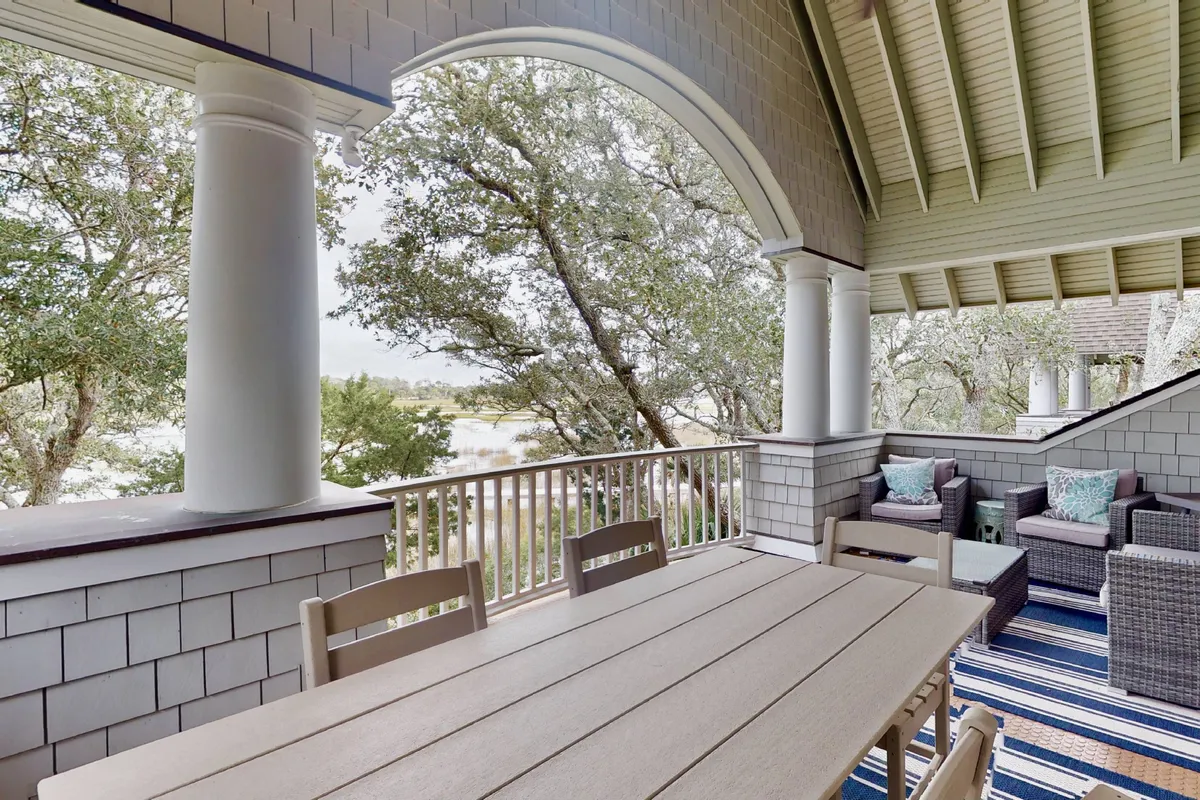 A screened-in patio with a dining table and lounge seating overlooks natural scenery through distinctive arches. The space is designed for outdoor dining, relaxing with friends, or enjoying the breeze while remaining shielded from insects and wind. The setting is equally suited to morning coffee or evening star-gazing.